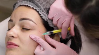 Yüz enjeksiyonu. Kozmetik Salonunda Yaşlanma Karşıtı Biorevalizasyon. Genç kız Hyaluronic asit derisi alıyor. Şırınga Kapalı Güzellik Elleri.