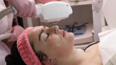 Gülümseyen kadın ELOS cilt yenileme yüz bakımı yapıyor. Yüzünde soğutma jeli ve lazer koruyucu gözlüklü bir kadın güzellik kliniğinde yalan söyleyen bir terapi masası, cildini lekelerden tedavi eden, yüz gerdirme ameliyatı yapan bir kadın..