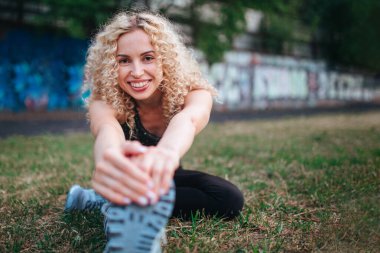 Genç, kıvırcık, atletik yapılı bir sarışın stadyumda antrenmandan önce ısınma turu yapıyor. Açık hava sporları