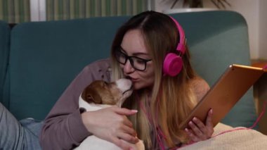 Kanepede bir kız dizüstü bilgisayarında bir köpekle uzanıyor ve kulaklıkla müzik dinliyor. İnternet üzerinden serbest çalışma ve iletişim. 