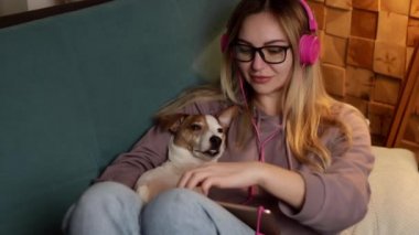 Kanepede bir kız dizüstü bilgisayarında bir köpekle uzanıyor ve kulaklıkla müzik dinliyor. İnternet üzerinden serbest çalışma ve iletişim. 