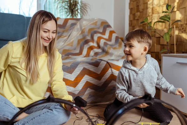 Mom and little son play racing on the carpet at home, have fun and hug. Single mother raises her son by playing cars