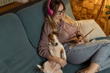 Kanepede bir kız dizüstü bilgisayarında bir köpekle uzanıyor ve kulaklıkla müzik dinliyor. İnternet üzerinden serbest çalışma ve iletişim