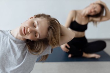 İki atletik çekici kız içerde yoga minderinin üzerinde lotus pozisyonunda otururlar. Yoga, spor ve sağlıklı yaşam tarzı.. 