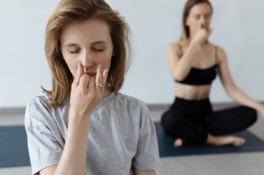 İki atletik çekici kız içerde yoga minderinin üzerinde lotus pozisyonunda otururlar. Yoga, spor ve sağlıklı yaşam tarzı.. 