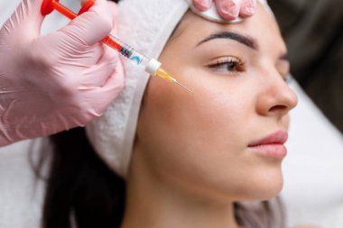 Kozmetik uzmanı güzel bir kadının yüzüne kırışıklık önleyici iğneler yapıyor. Güzellik salonunda kadın estetiği.