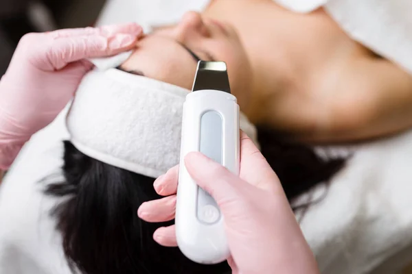 Facial cleansing with ultrasound scrubber. Woman receiving ultrasound facial peeling and cleansing. Cosmetology and face skin care. Facial treatment.