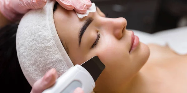 Facial cleansing with ultrasound scrubber. Woman receiving ultrasound facial peeling and cleansing. Cosmetology and face skin care. Facial treatment.