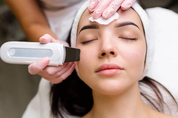 Facial cleansing with ultrasound scrubber. Woman receiving ultrasound facial peeling and cleansing. Cosmetology and face skin care. Facial treatment.