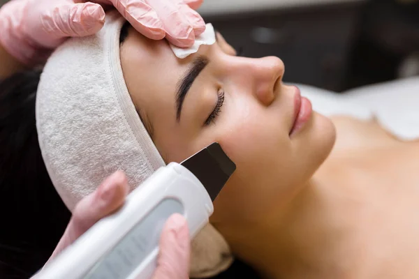 Facial cleansing with ultrasound scrubber. Woman receiving ultrasound facial peeling and cleansing. Cosmetology and face skin care. Facial treatment.