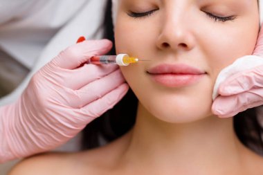 Bir kozmetoloji salonunda dudak şekli düzeltme prosedürü. Uzman, hastanın dudaklarına bir iğne yapar. Dudak büyütme