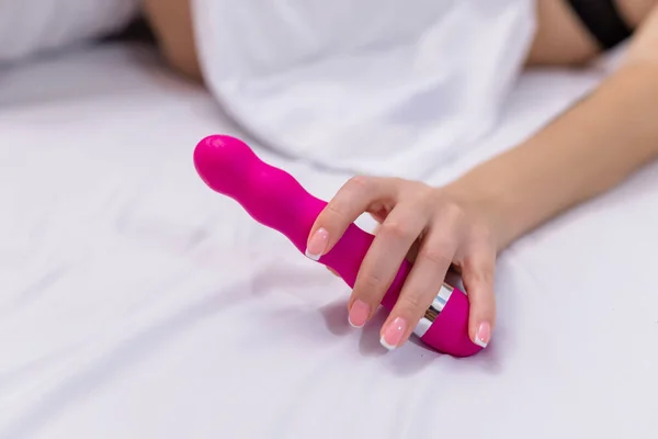 Woman in bed under sheets holding vibrator in hand. High quality photo