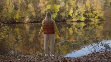 Güzel sarışın kadın nehir kenarında duruyor ve manzaranın tadını çıkarıyor.. 