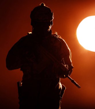 Özel Harekat Kuvvetleri Saldırı Tüfeği 'ni elinde tutan Koruyucu Muharebe Üniformalı ordu askeri gün batımında hareket ediyor akşam güneşiyle aydınlanıyor
