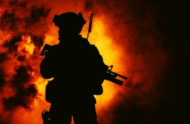 Modern piyade askerlerinin silueti, taktiksel cephane ve miğfer giymiş seçkin ordu savaşçıları, ateş ve duman içinde saldırı tüfeğiyle ayakta duruyor.