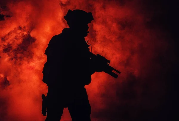 現代の歩兵兵士のシルエット 戦術的な弾薬やヘルメットのエリート軍の戦闘機 火災や煙の中で手にアサルトサービスライフルで立って — ストック写真