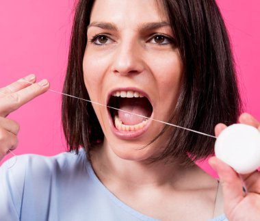 Güzel genç bir kadın pembe arka planda diş ipi kullanıyor.