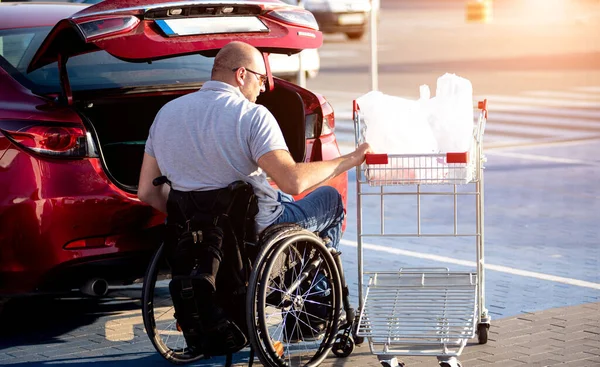 Person med en fysisk funktionsnedsättning lägger inköp i bagageutrymmet på en stormarknad parkeringsplats — Stockfoto