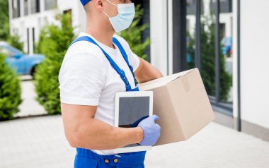 Koruyucu maske takan ve eldiven takan genç kurye karantina sırasında mal teslim ediyor.