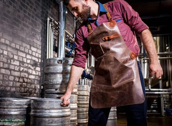Cervecero joven masculino en delantal de cuero sostiene barril con cerveza artesanal en fábrica de cerveza moderna — Foto de Stock
