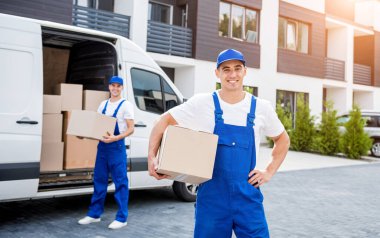 İki nakliye şirketi çalışanı minibüsten yeni eve kutular boşaltıyor.