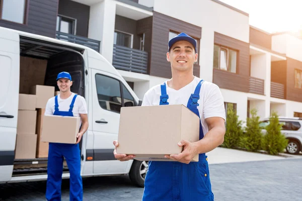 Dos trabajadores de la empresa de mudanzas descargan cajas de minibús en un nuevo hogar —  Fotos de Stock