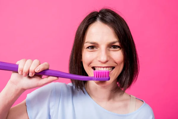 Schöne glückliche junge Frau mit großer Zahnbürste auf leerem rosa Hintergrund — Stockfoto