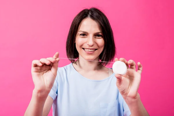 Schöne junge Frau verwenden Zahnseide auf rosa Hintergrund — Stockfoto