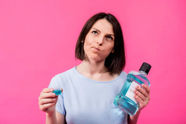 Schöne Mädchen benutzt Mundwasser auf dem rosa Hintergrund — Stockfoto