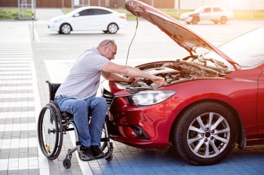 Fiziksel engelli kişi arabasını park yerinde kontrol ediyor.