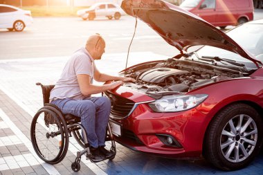 Fiziksel engelli kişi arabasını park yerinde kontrol ediyor.