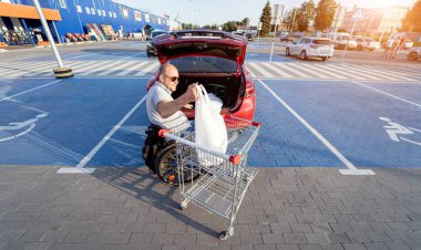 Fiziksel engelli biri alışverişi süpermarketin otoparkında bir arabanın bagajına koyar.