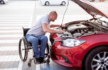 Fiziksel engelli kişi arabasını park yerinde kontrol ediyor.