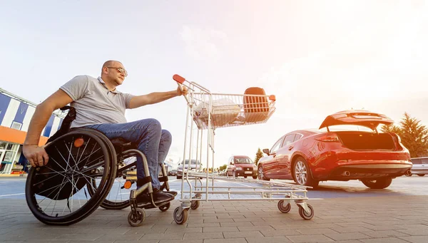 Person med en fysisk funktionsnedsättning driver vagn framför sig själv på snabbköpsparkering — Stockfoto