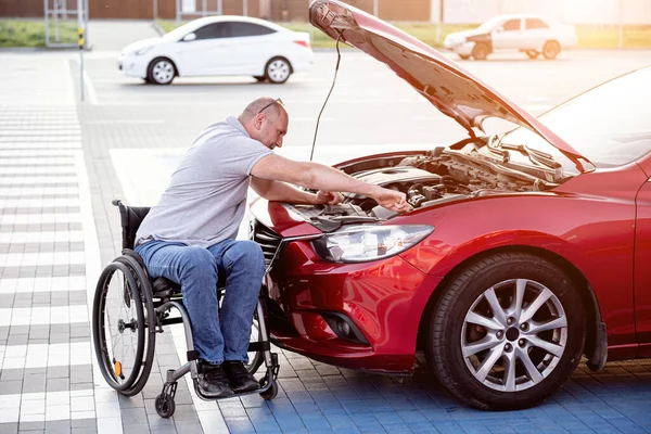 Fiziksel engelli kişi arabasını park yerinde kontrol ediyor.