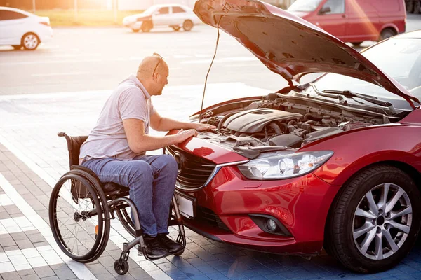 Fiziksel engelli kişi arabasını park yerinde kontrol ediyor.