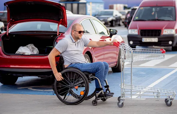 Persona con una discapacidad física pone compras en el maletero de un coche en un estacionamiento de supermercados —  Fotos de Stock