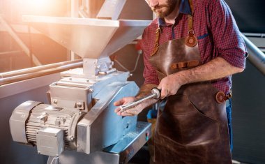Deri önlüklü genç bir bira üreticisi modern bir bira fabrikasında malt tohumlarının öğütülmesini kontrol eder.