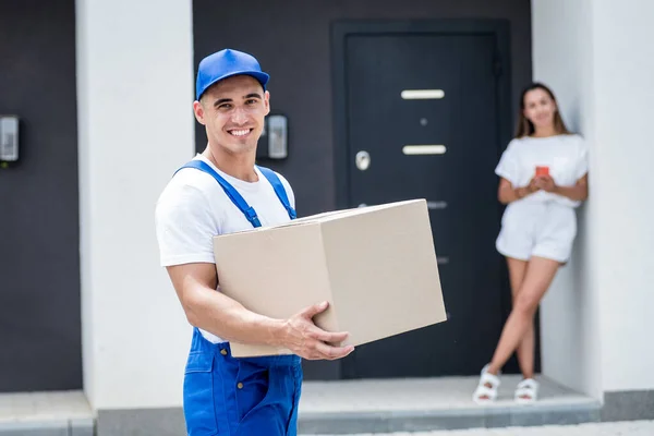 Joven mensajero entregando mercancías a una joven en casa —  Fotos de Stock