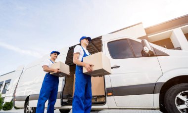 İki nakliye şirketi çalışanı minibüsten müşterilerin evlerine kutu indiriyor.