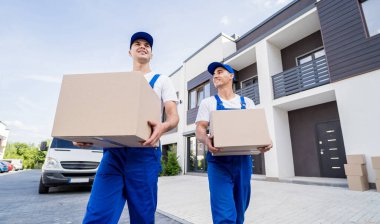 İki nakliye şirketi çalışanı minibüsten müşterilerin evlerine kutu indiriyor.