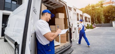 İki nakliye şirketi çalışanı minibüsten kutuları ve mobilyaları boşaltıyor.