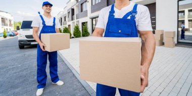 İki nakliye şirketi çalışanı minibüsten müşterilerin evlerine kutu indiriyor.