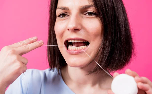 Wanita muda yang cantik menggunakan benang gigi pada latar belakang merah muda — Stok Foto