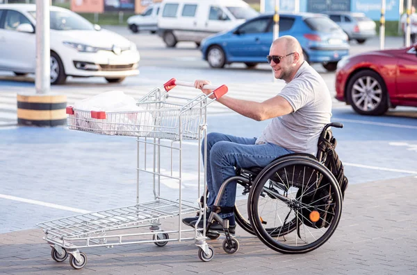 Fiziksel engelli bir insan süpermarketin önünde el arabasını itiyor. — Stok fotoğraf