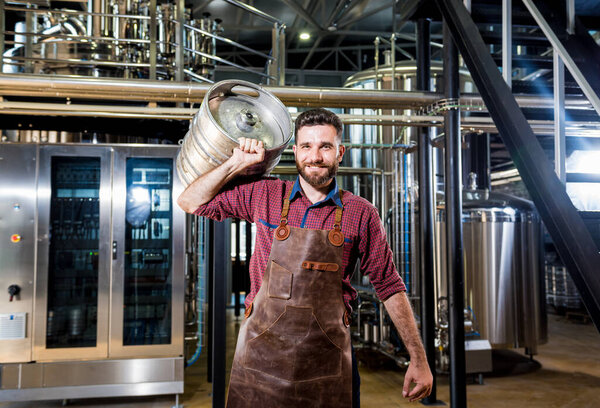 Молодой пивовар в кожаном фартуке держит бочку с ремесленным пивом на современном пивоварне