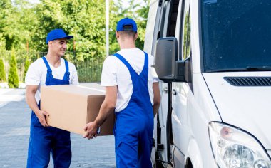 İki nakliye şirketi çalışanı bir minibüse kutu yüklüyorlar..