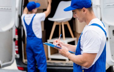 İki nakliye şirketi çalışanı minibüsten yeni eve kutular boşaltıyor.