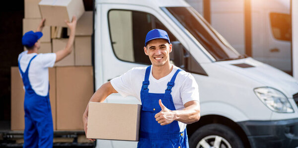 Two removal company workers unloading boxes from minibus into new home