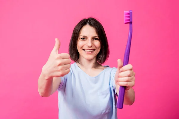 Schöne glückliche junge Frau mit großer Zahnbürste auf leerem rosa Hintergrund — Stockfoto